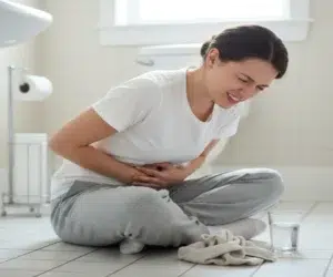 Mulher sentada no chão do banheiro com dor de barriga.